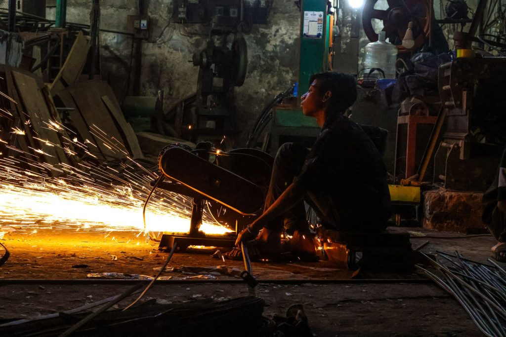 Worker in a dimly lit industrial workshop with sparks flying