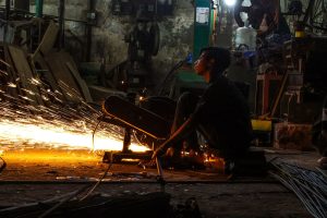 Worker in a dimly lit industrial workshop with sparks flying