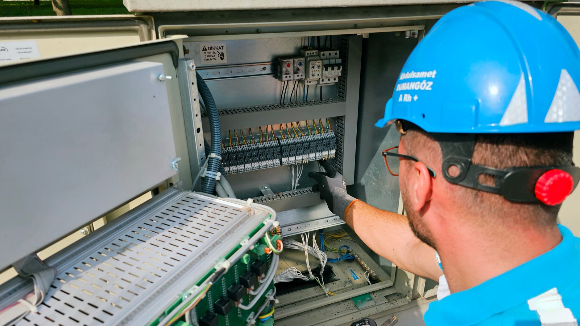 Electrician wearing PPE including hard hat, glasses, and hearing protection while working on an electrical panel