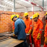 Manufacturing supervisors in hard hats and high-visibility vests talking on a workshop floor