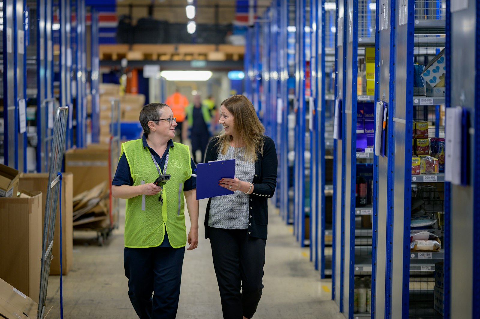 Two staff reviewing a clipboard while walking through warehouse parts shelving