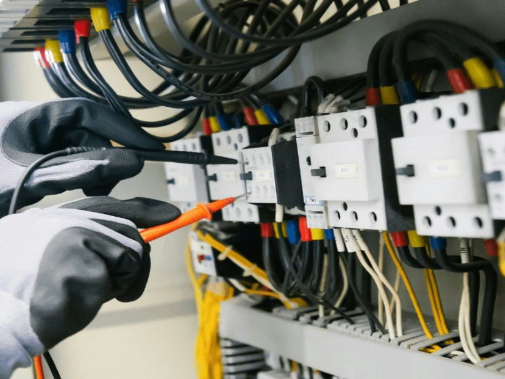 Electrician testing electrical equipment and wiring inside an industrial control panel