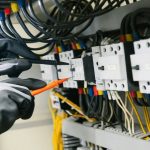 Electrician testing electrical equipment and wiring inside an industrial control panel