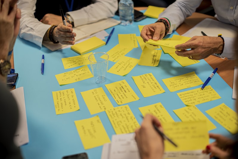 Hands arranging yellow sticky notes across a table during an improvement workshop