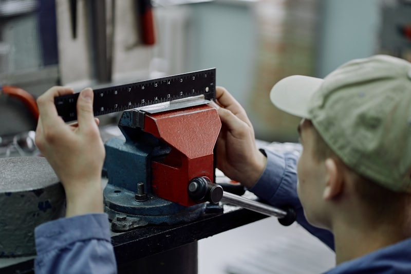 Worker measuring a metal part clamped in a vice using a steel rule