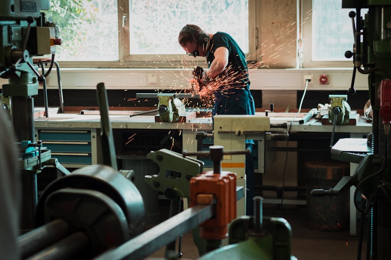 Worker shaping a metal part at a bench in an industrial workshop