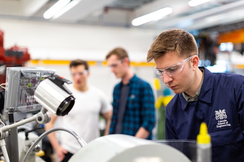 Engineers in safety glasses working together on a machine in a manufacturing workshop