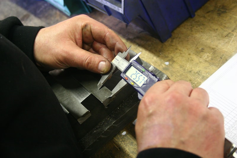 Hands measuring a machined part with digital calipers