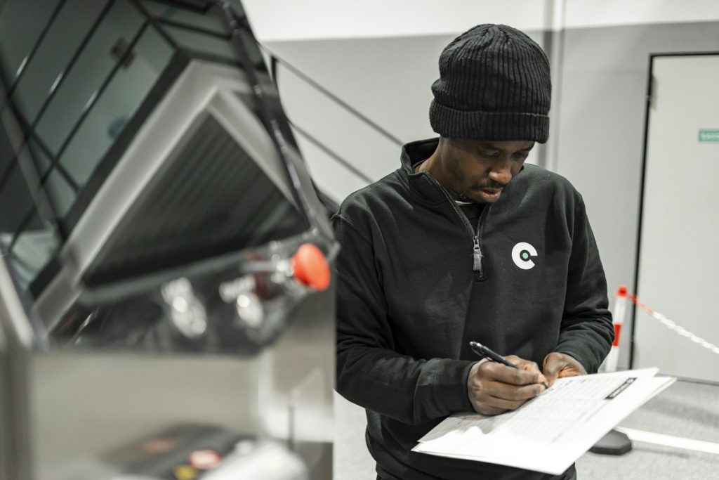 Manufacturing technician completing a structured check sheet beside an industrial machine
